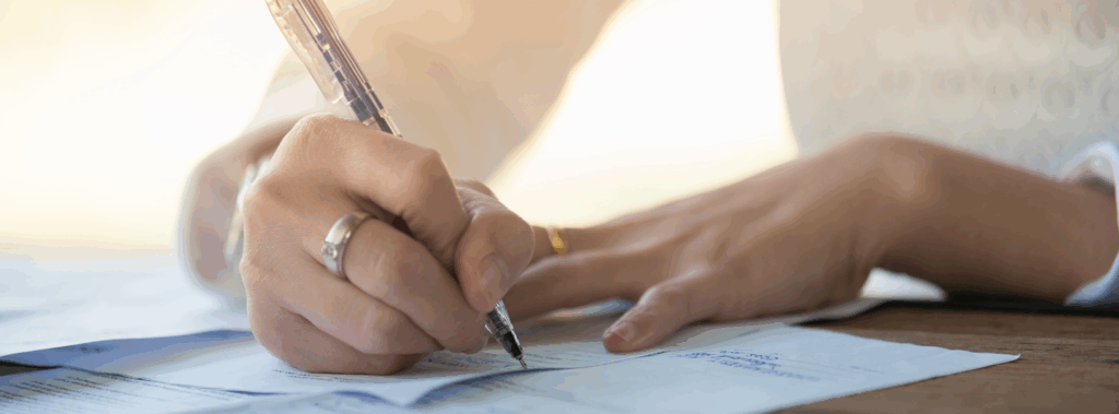 Zwei Hände im Schreibvorgang, einer hält einen Stift und schreibt damit auf Papierunterlage.